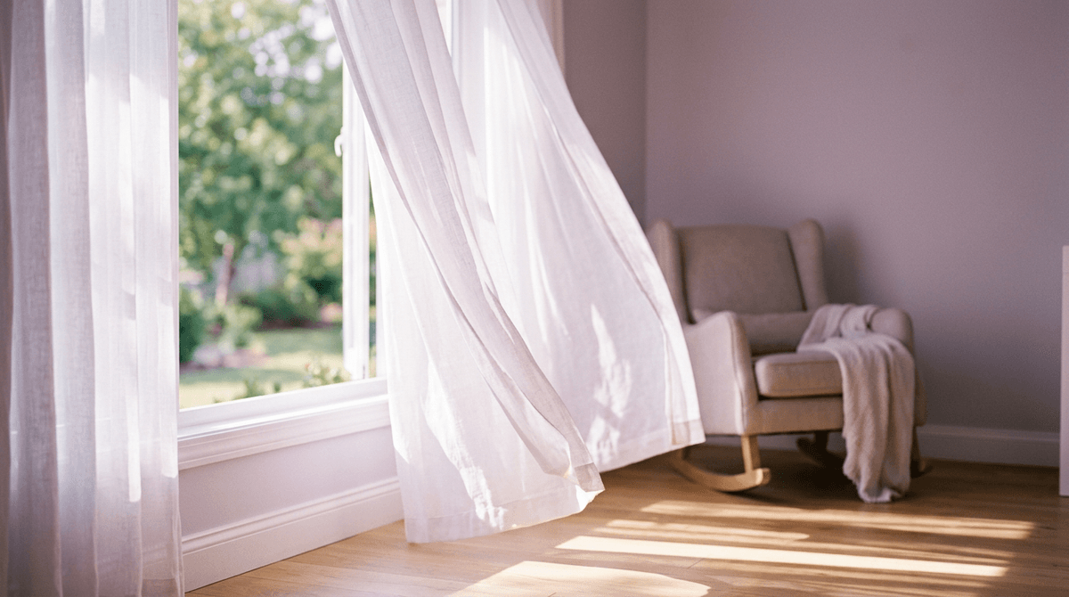 Sheer white curtains blowing in a sunlit nursery with a rocking chair, symbolizing letting go of pressure