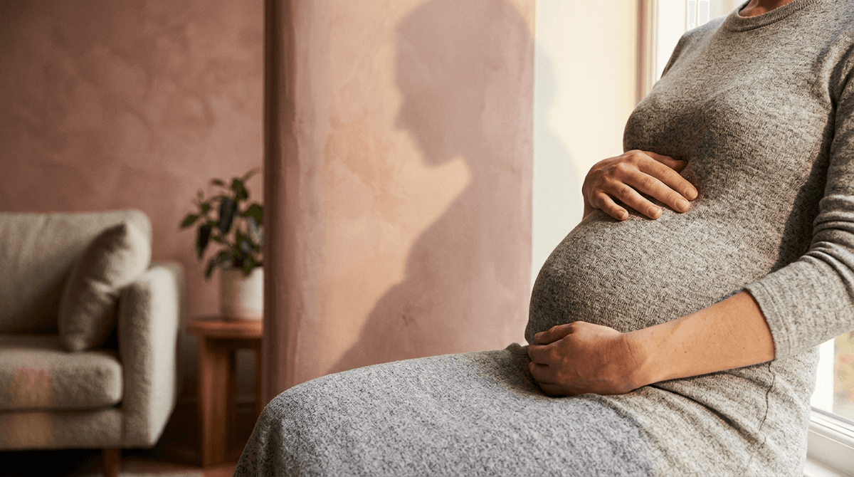 A soft silhouette of a pregnant woman against a warm wall fading into bright light