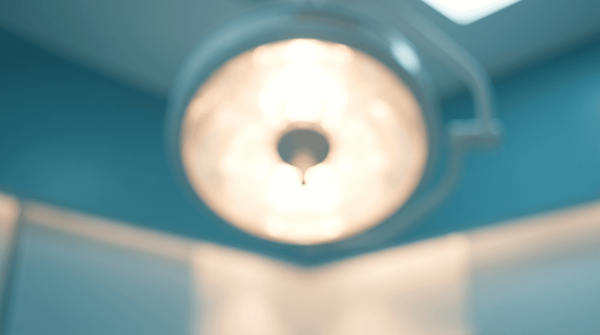 The warm circular glow of an overhead surgical lamp, softly blurred to feel like a warm sun